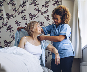 Youn nurse helping older woman dress