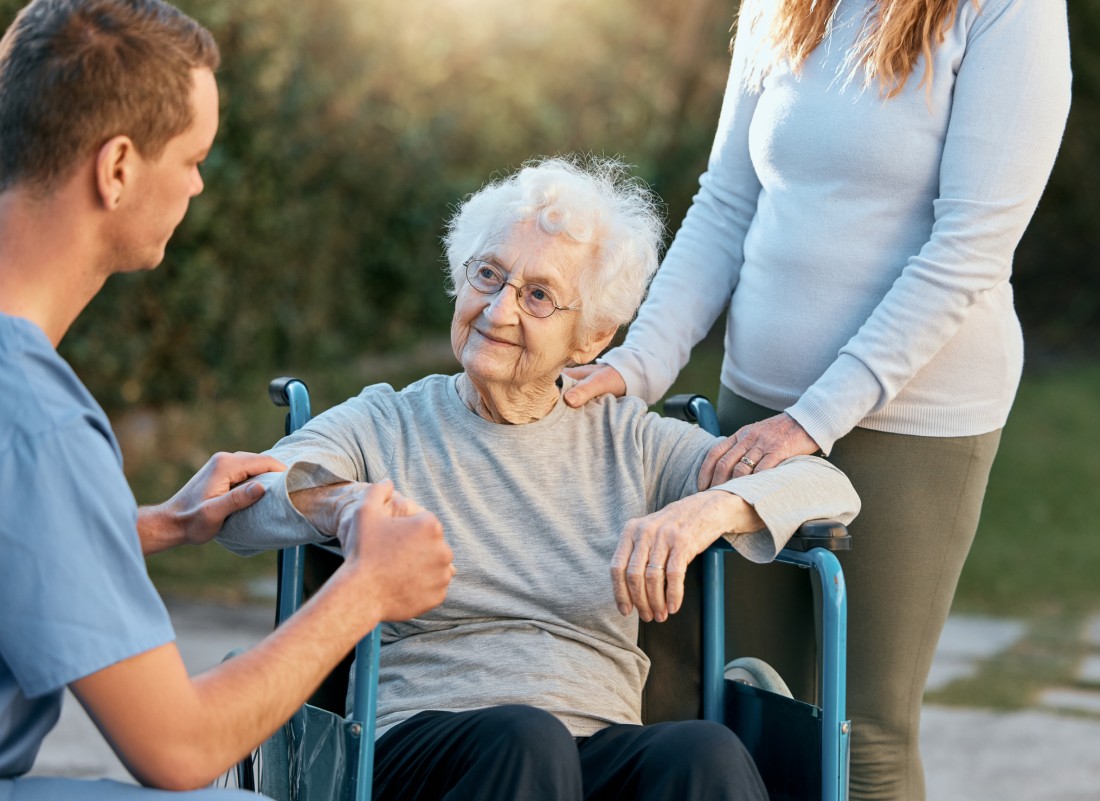 An older woman in a wheelchair is surrounded by both her family and her caregiver