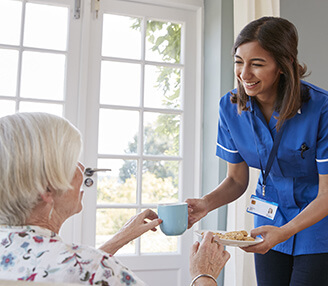 Young nurse giving tea and treat to older woman